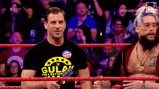 two men are standing in a wrestling ring with a microphone in their hands .