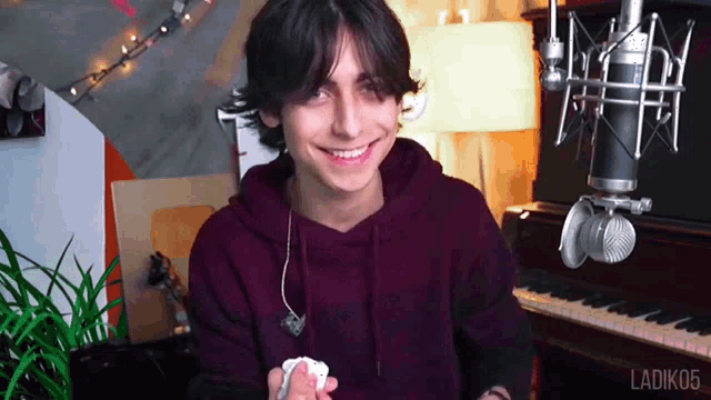 a young man in a purple hoodie is smiling in front of a microphone and a piano .