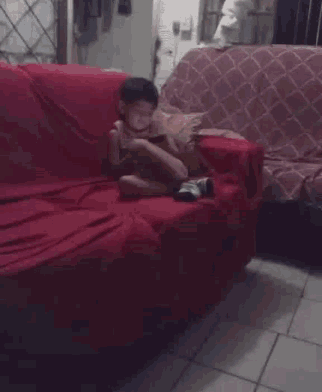 a little boy is sitting on a red couch looking at his phone