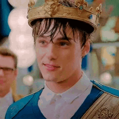 a young man wearing a crown and a blue vest is looking at the camera .