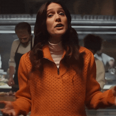 a woman in an orange sweater is adjusting her sweater
