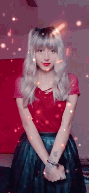 a woman wearing a red shirt and a black skirt is standing in front of a pink wall .