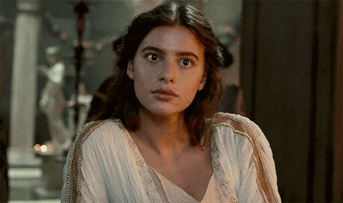 a woman in a white dress looks at the camera with a serious look on her face