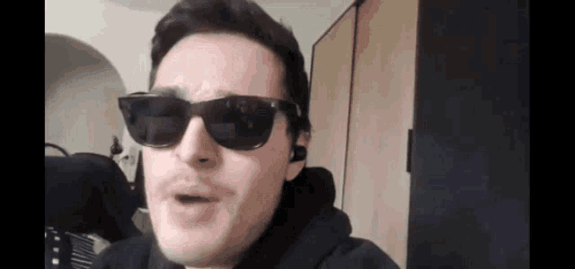a man wearing sunglasses and a black hoodie is making a face .