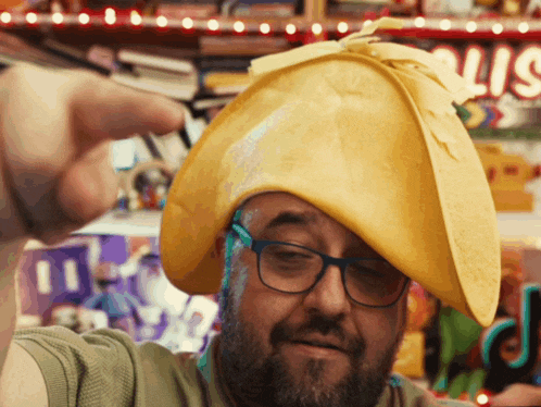 a man wearing glasses and a yellow hat is pointing at the camera