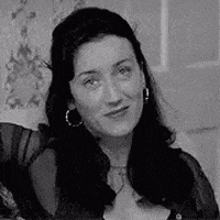a woman wearing hoop earrings is sitting on a bed in a black and white photo .