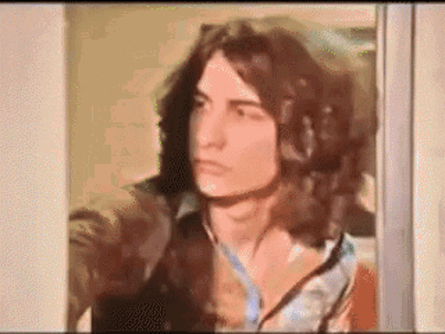 a man with long hair is standing in front of a door and looking out .