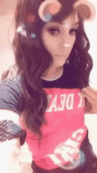 a woman wearing a pink shirt with the word devil on it takes a selfie .
