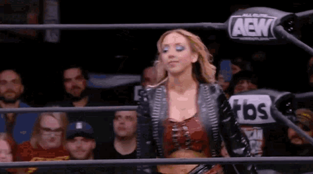 a woman is standing in a wrestling ring in front of a crowd of people .