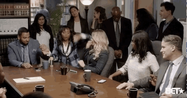 a group of people are sitting around a conference table with a phone on it .