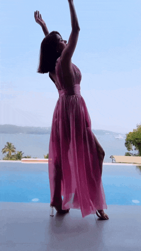 a woman in a pink dress is standing in front of a swimming pool