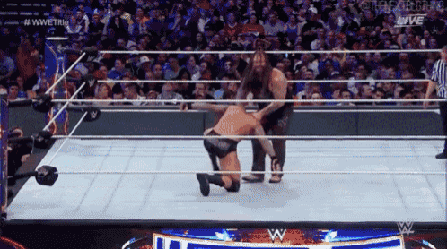 a wrestler is kneeling down in a wrestling ring while a referee looks on .