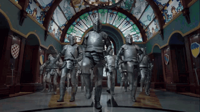 a group of knights are walking in a hallway with a stained glass window behind them