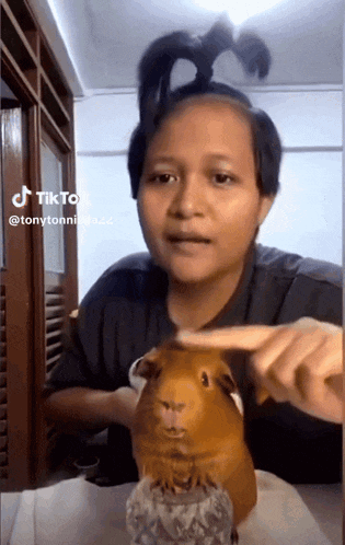 a woman is petting a guinea pig while wearing a ponytail