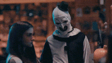 a man in a clown costume is standing next to a woman in a pumpkin patch .