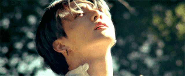 a close up of a person 's face with the sun shining through the trees