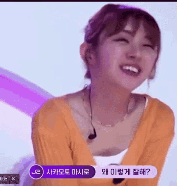 a woman wearing an orange sweater and a necklace is smiling while sitting on a stage .