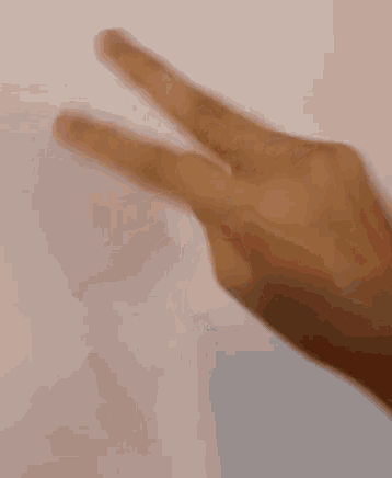 a close up of a person 's hand making a heart shape with their fingers against a white wall .