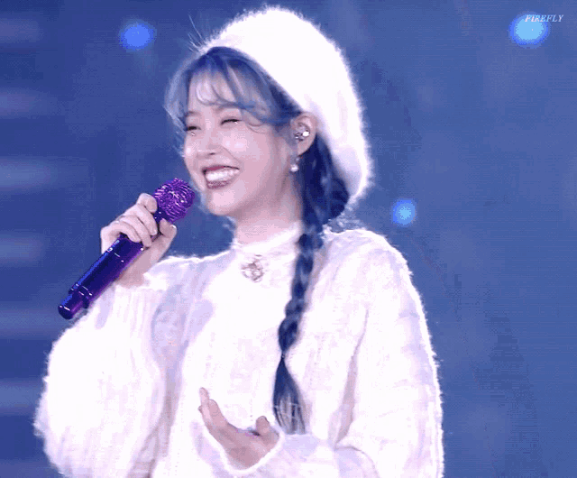 a woman wearing a white sweater and a white hat is holding a purple microphone and smiling