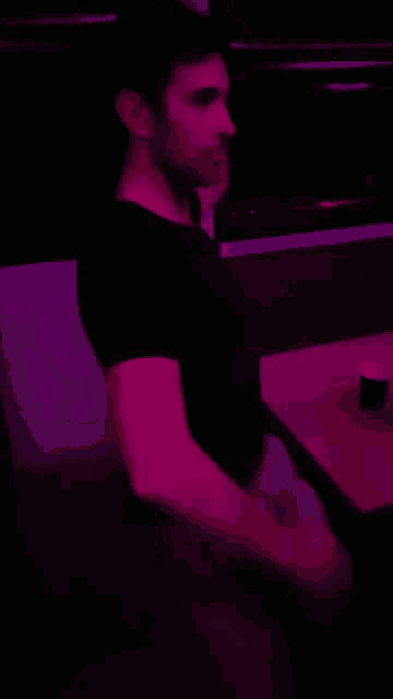 a man in a black shirt is standing in a dark room with pink lights