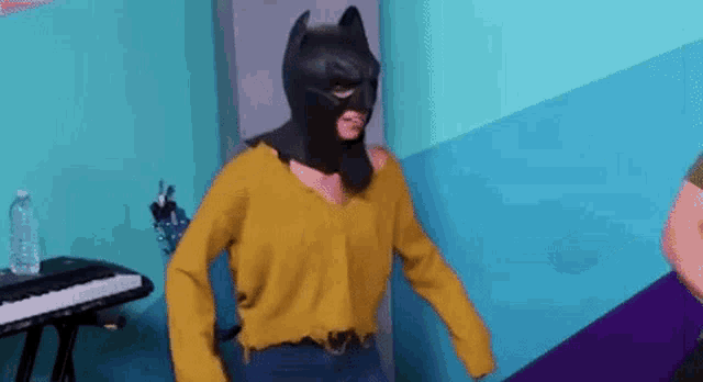 a person wearing a batman mask and a yellow sweater is standing in a room .