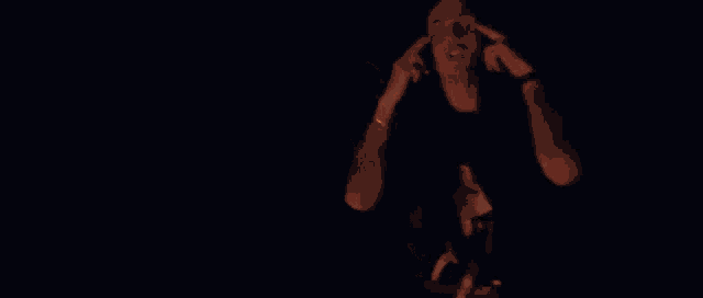 a man in a black shirt is standing in front of a fire in the dark .