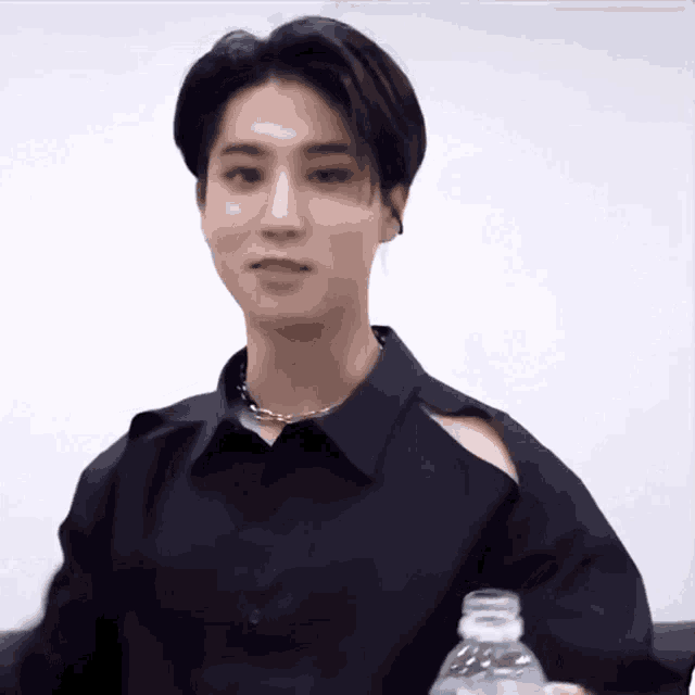 a young man is wearing a black shirt with a cut out on the shoulder and holding a bottle of water .