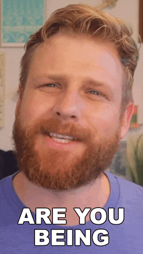 a man with a beard is smiling with the words are you being behind him