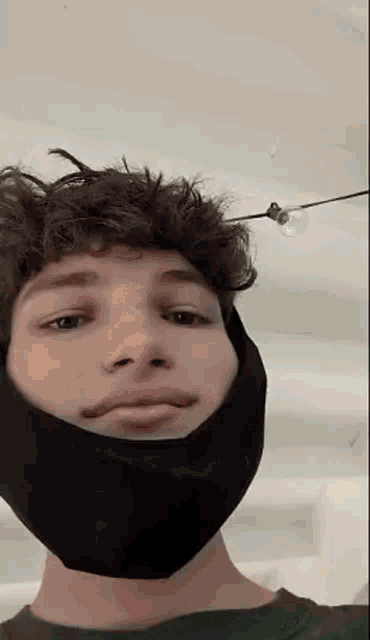a young man wearing a black mask on his face is taking a selfie .