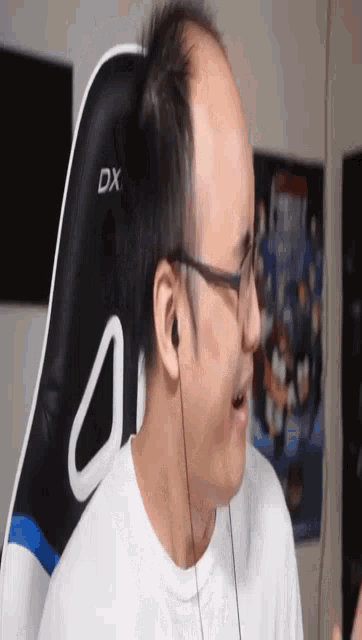 a man wearing glasses is sitting in a black and white dx gaming chair