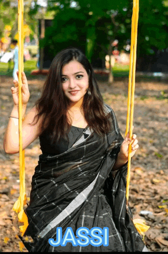 a woman in a black saree is sitting on a yellow swing and the name jassi is on the bottom