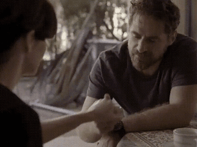 a man and a woman are sitting at a table and holding hands