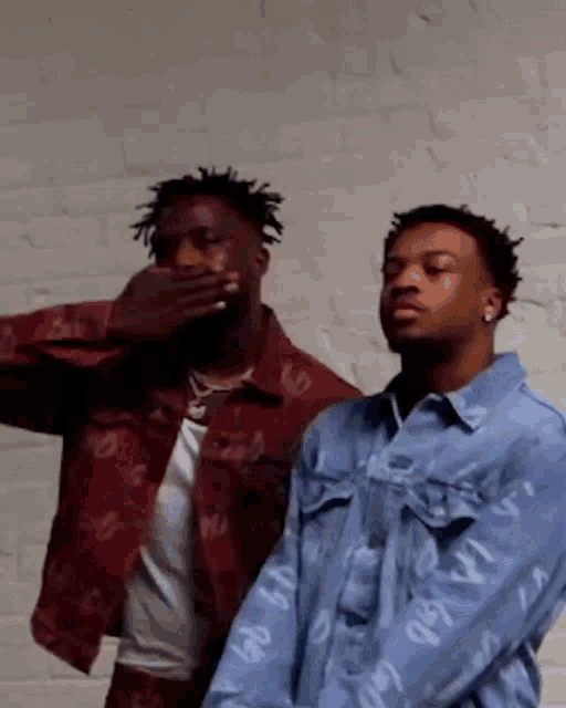 two men are standing next to each other and one of them is covering his mouth .