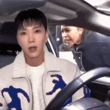 a man in a white jacket is driving a car while another man looks on .
