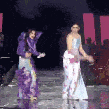 two women are dancing on a stage and one is wearing a purple dress