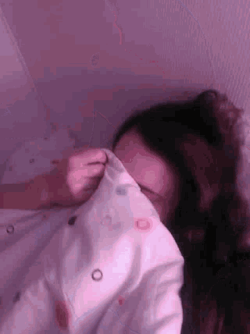 a woman is laying on her back in a bed with a pink blanket on her head .
