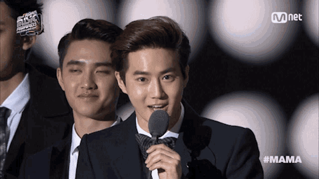 a man in a suit speaking into a microphone with the hashtag mama on the bottom