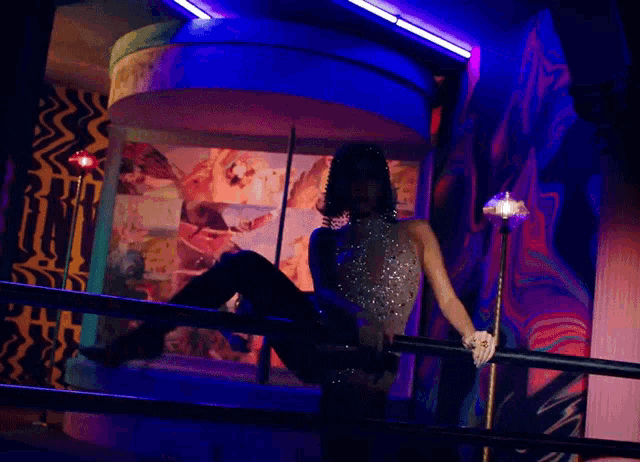 a woman is sitting on a railing in a dark room with a colorful background .