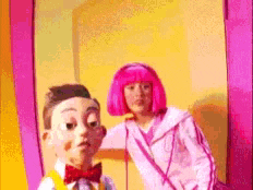 a girl with pink hair is standing next to a puppet