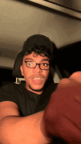 a man wearing glasses and a hat is sitting in a car and making a funny face