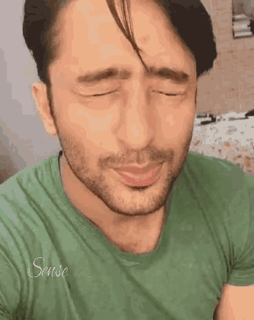 a man with a beard is wearing a green shirt and making a funny face with his eyes closed .