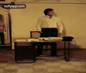 a man in a white shirt is standing in front of a desk with a phone on it .