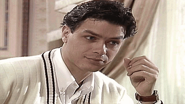 a man wearing a white sweater and a white shirt is sitting at a table
