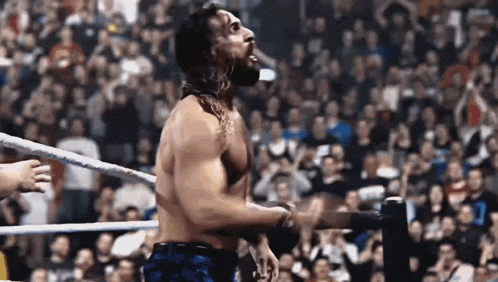 a man without a shirt is standing in a wrestling ring with a crowd behind him .