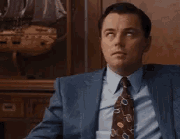 a man in a suit and tie is sitting in front of a wooden wall .