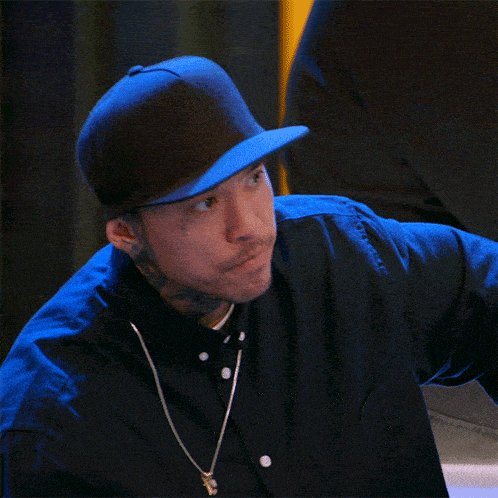 a man wearing a black shirt and a blue hat has a tattoo on his forehead