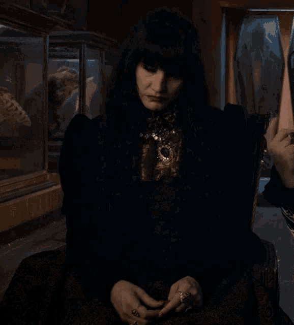 a woman in a black dress is sitting in a chair in a dark room