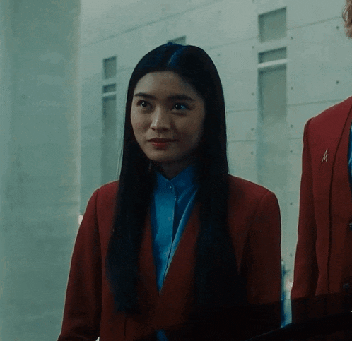 a woman wearing a red jacket and a blue shirt has the letter a on her lapel