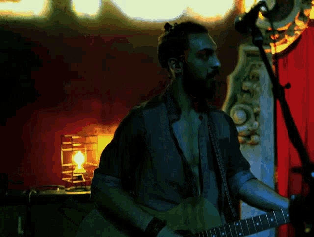 a man with a beard is playing a guitar in front of a red curtain with the letter l on it