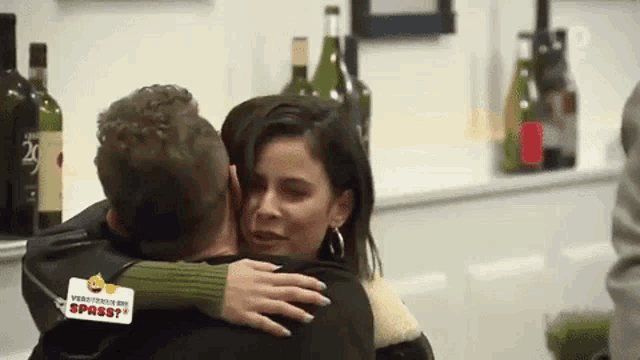 a man and a woman are hugging each other in a kitchen with bottles of wine in the background .